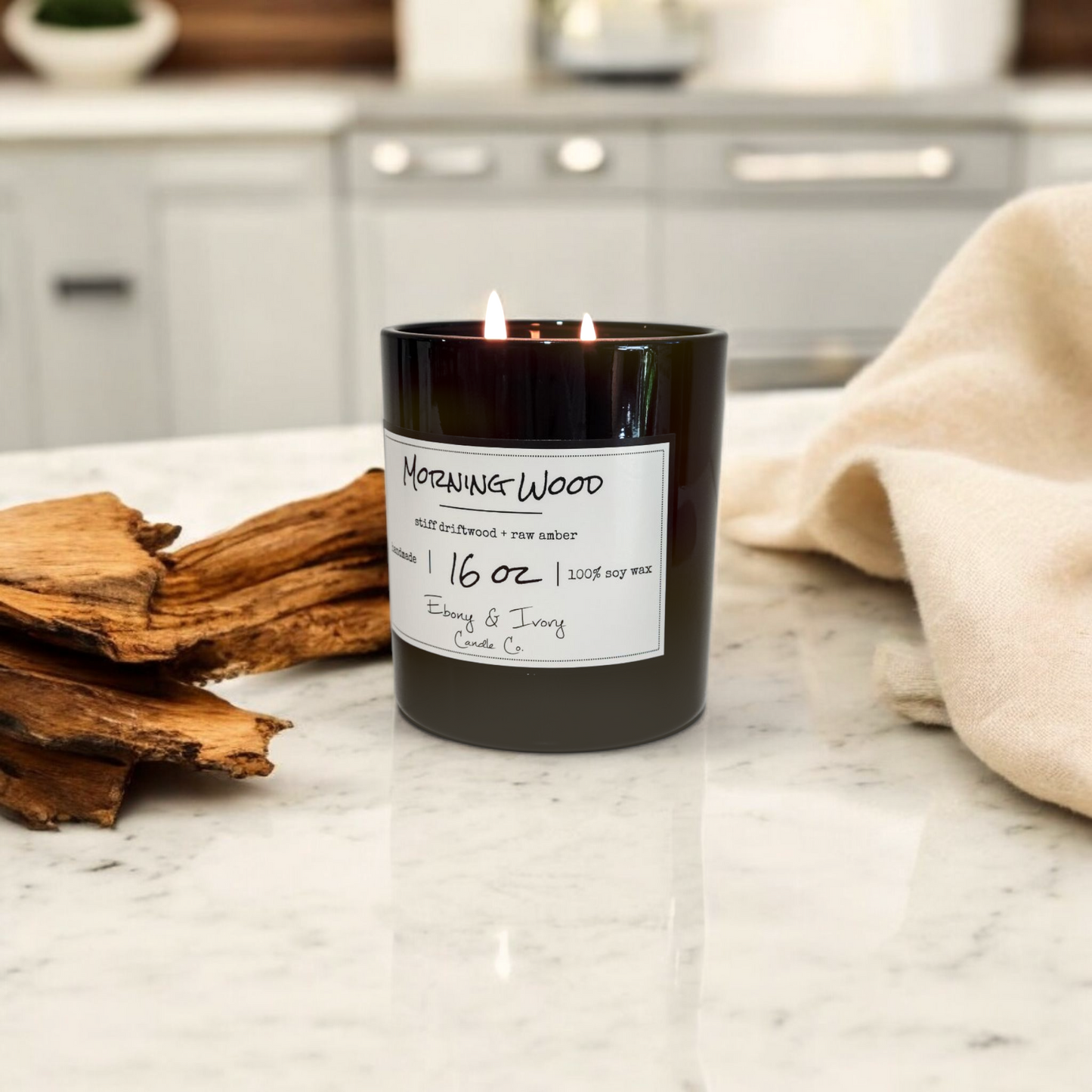 Candle labeled 'Morning Wood' on a marble countertop with drift wood and a towel.