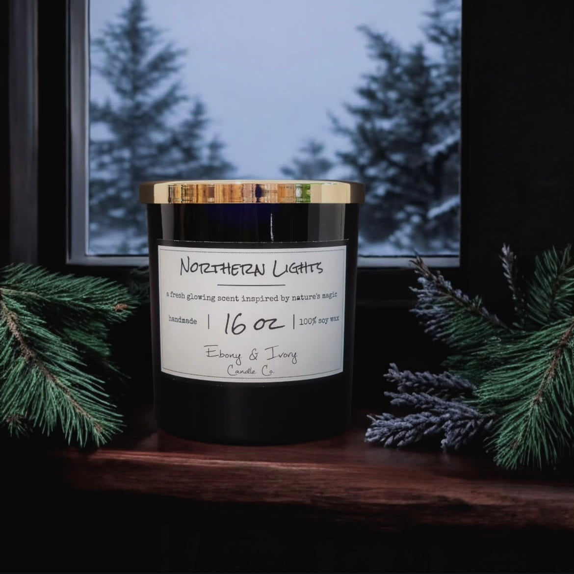 A black jar 16oz soy candle with a gold lid and a white label named Northern Lights, in a window sill during winter with pine branches and lavender beside it, made by Ebony & Ivory Candle Co in Lethbridge, Alberta, Canada