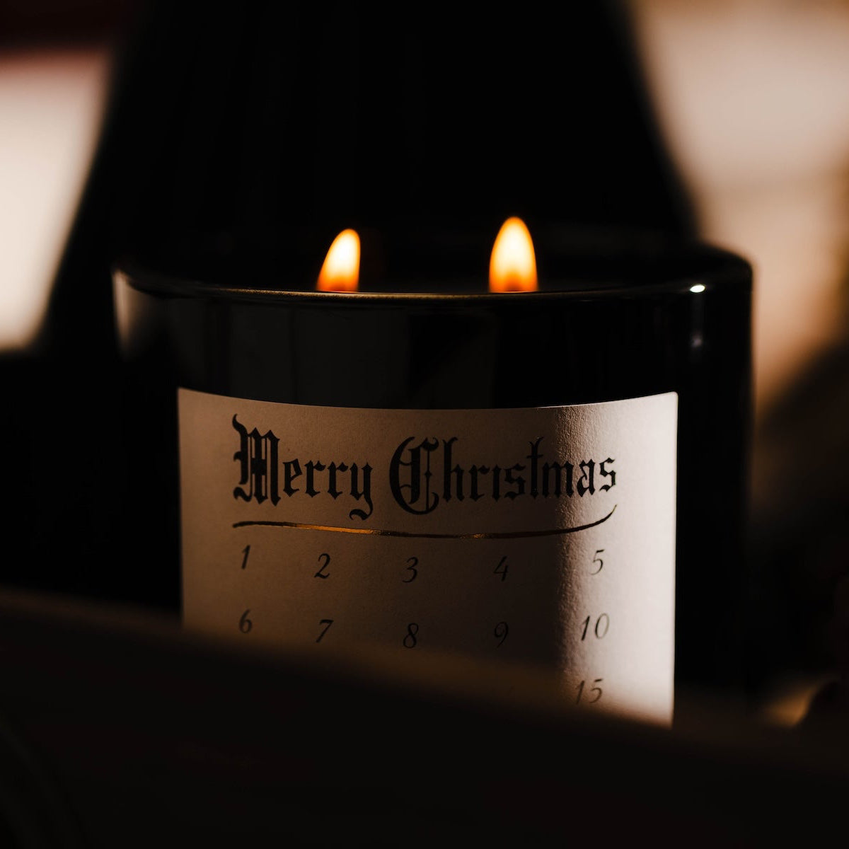 Candle with a 'Merry Christmas' label on wrapped presents with a blurred Christmas tree in the background. Advent Christmas countdown candle soy wax. #1 Christmas candle.