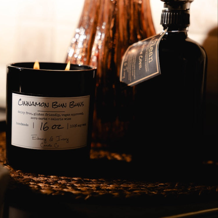 A black glass soy candle with a all purpose kitchen cleaner in a cozy setting.