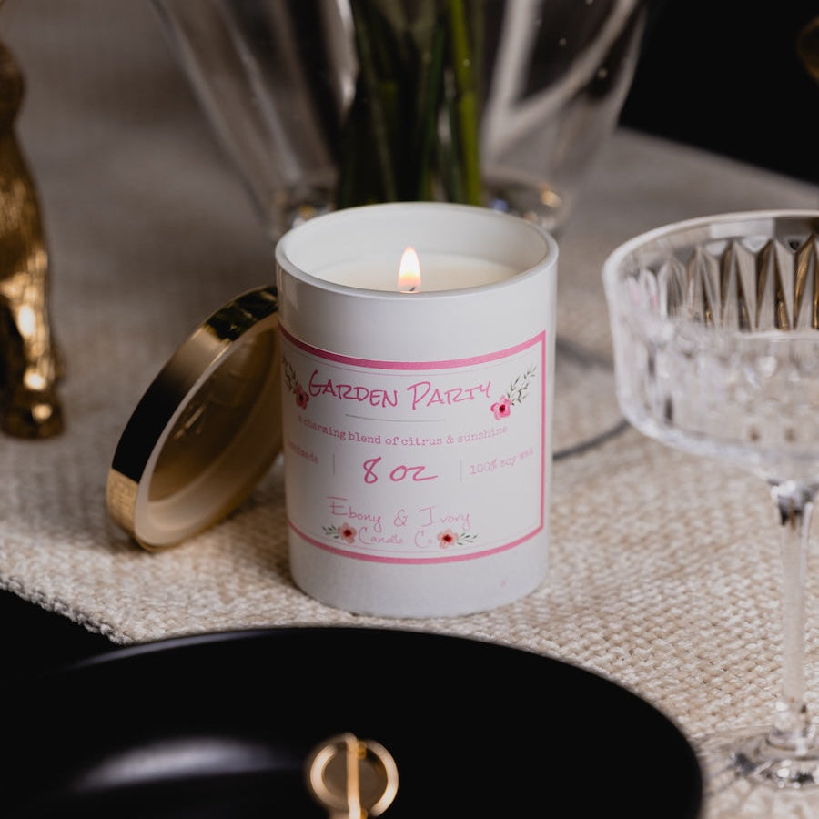 Candle in a decorative container with a label on a table with decorative items.