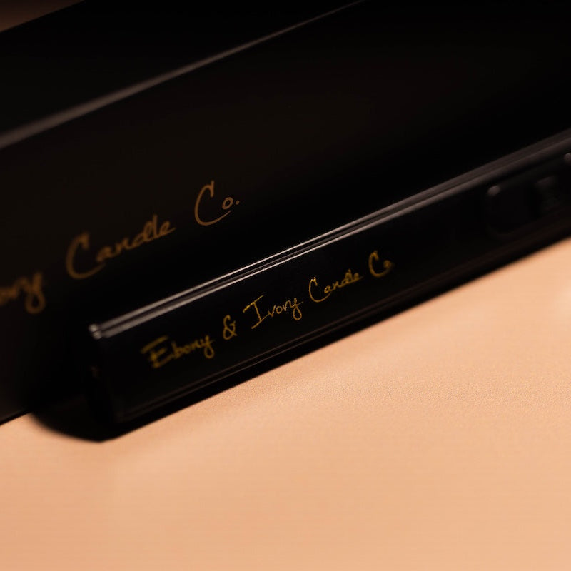 Close-up of a black product with 'Ebony & Ivory Candle Co.' branding on a beige background. black and gold usb lighter