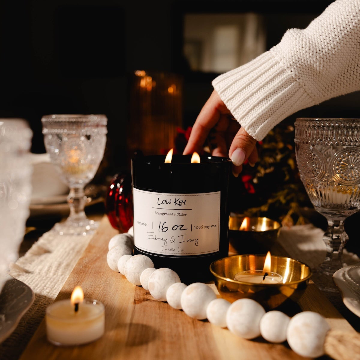 Person lighting a candle on a table with decorative items. Beautiful table setting with black vessel soy candle.