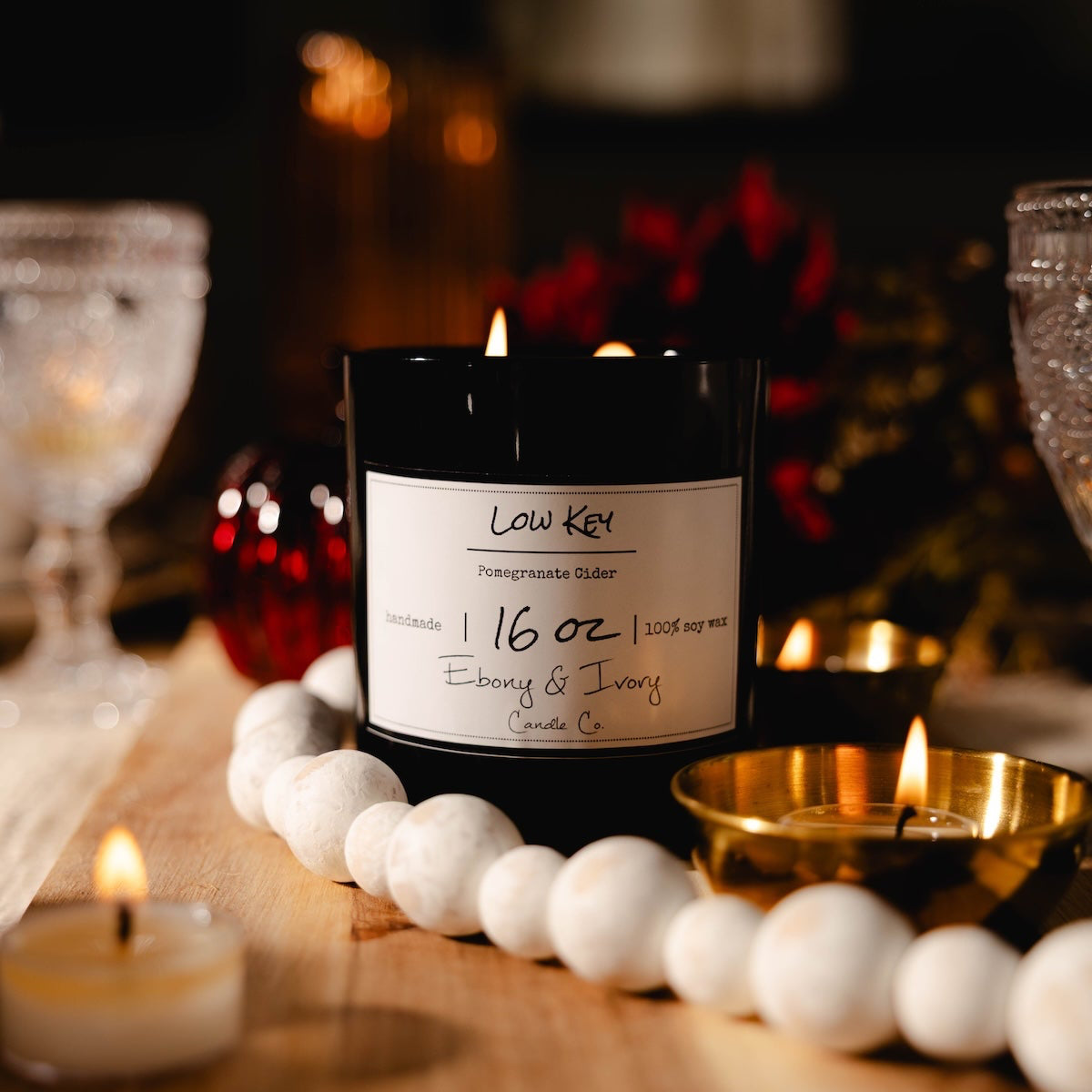 Candle with a label on a decorative table setting with other candles and lights. pomegranate cider candle, candle table setting.