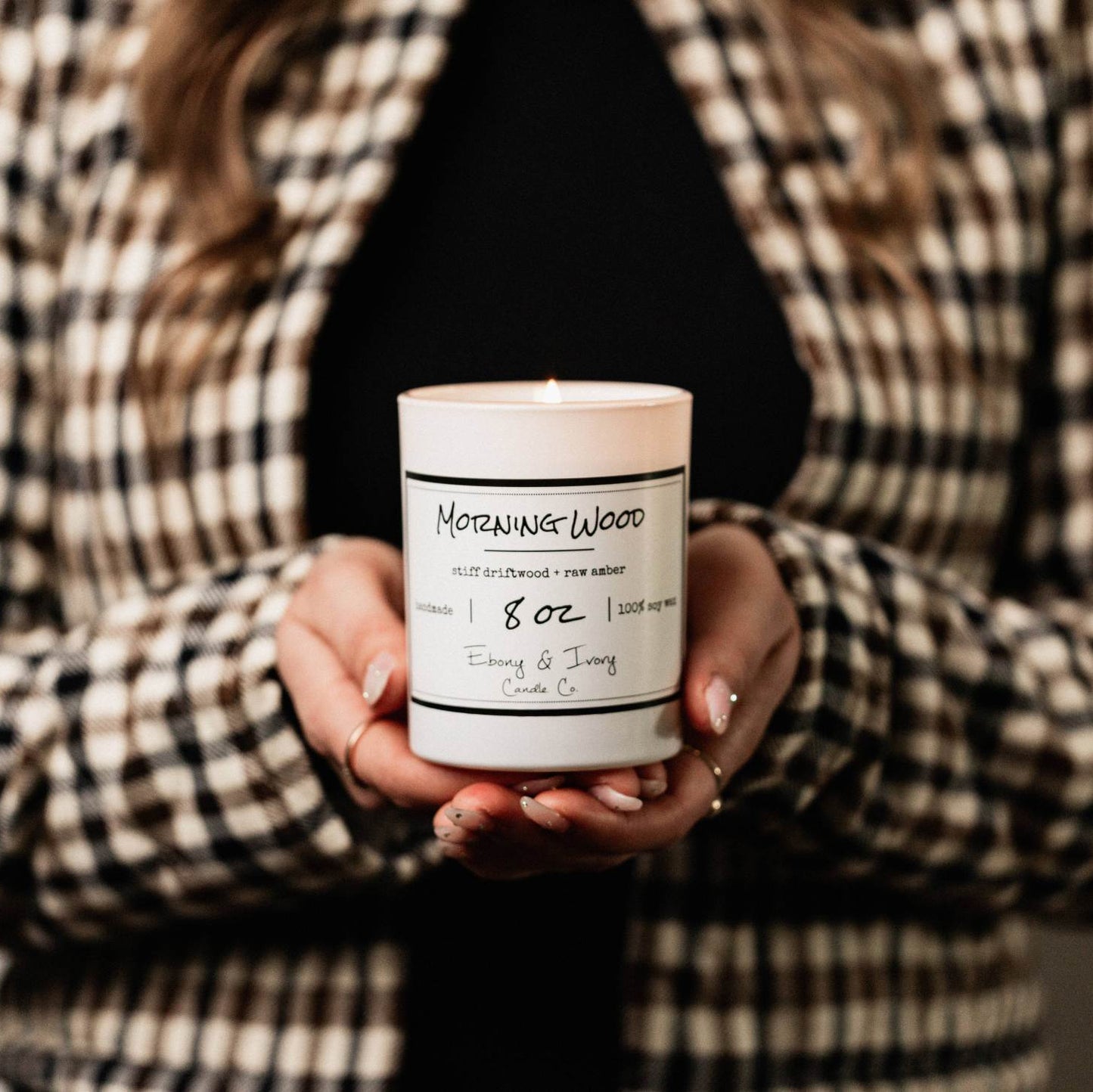 A white jar 8oz soy candle with a white label named Morning Wood, being held by a person wearing a black shirt and a checkered jacket, made by Ebony & Ivory Candle Co in Lethbridge, Alberta, Canada