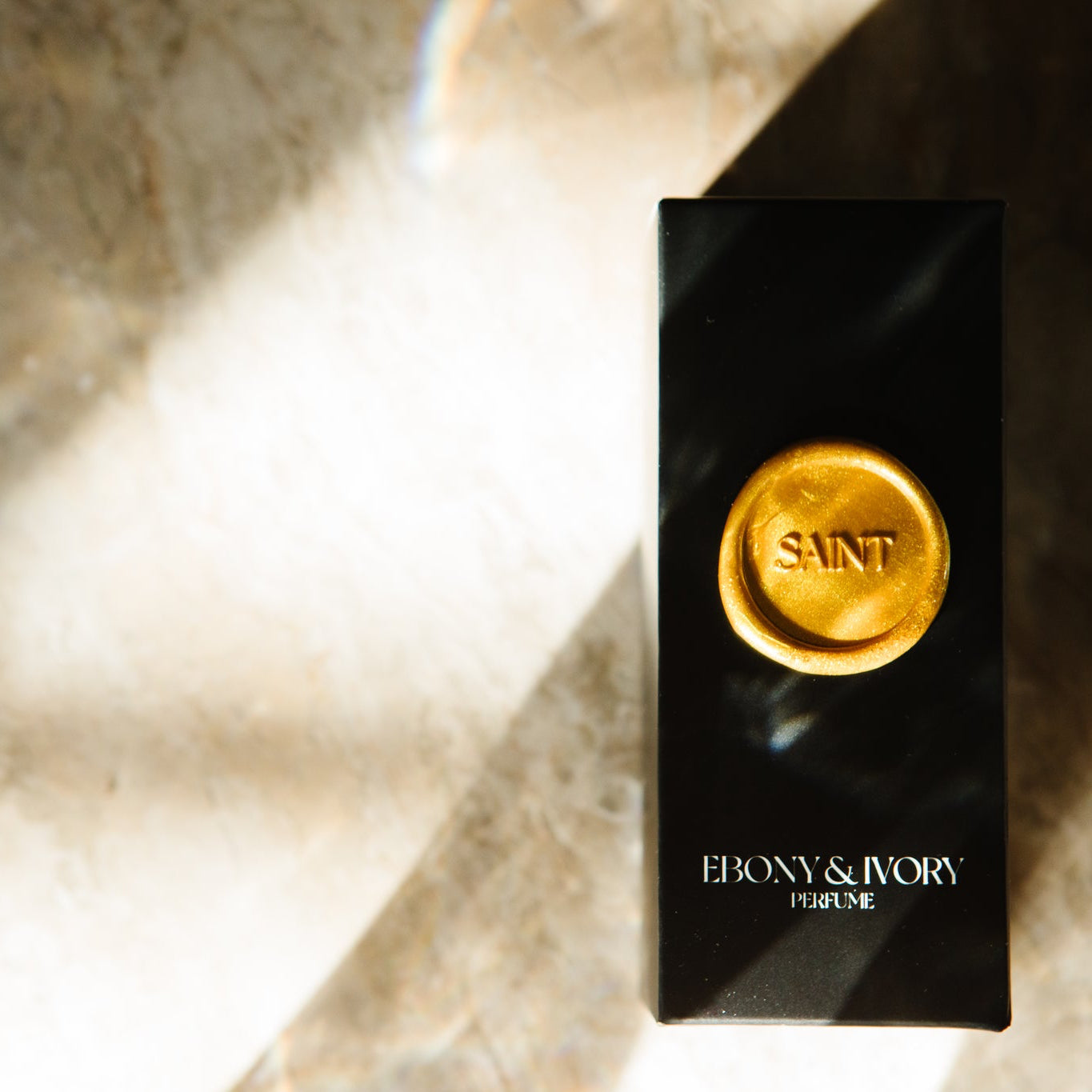 Black and gold product packaging with 'Saint Ebony & Ivory' branding on a textured surface.