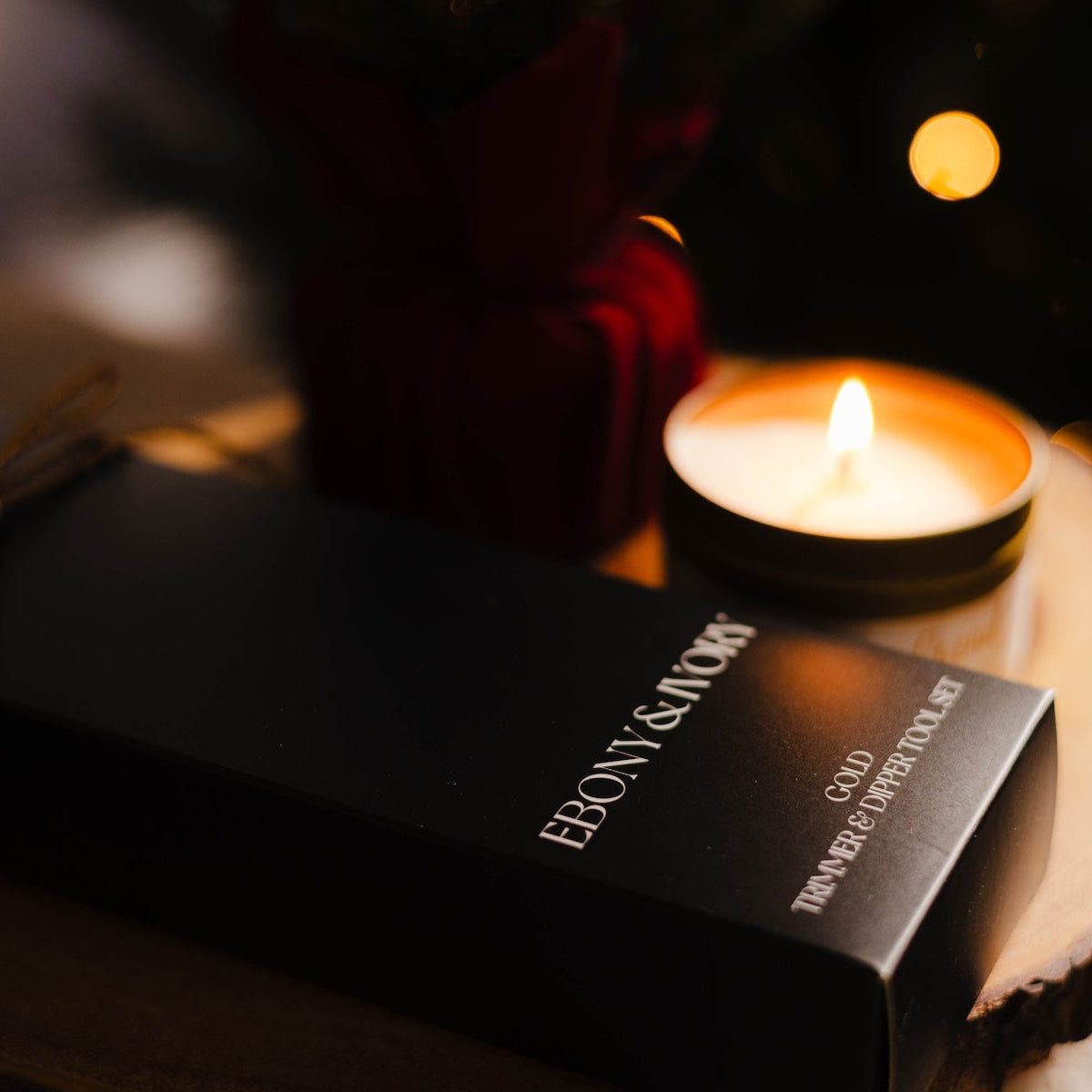 Ebony & Ivory product packaging with a lit candle on a dark background. Christmas candle in gold tin. Gold trimmer and dipper for candle tools.