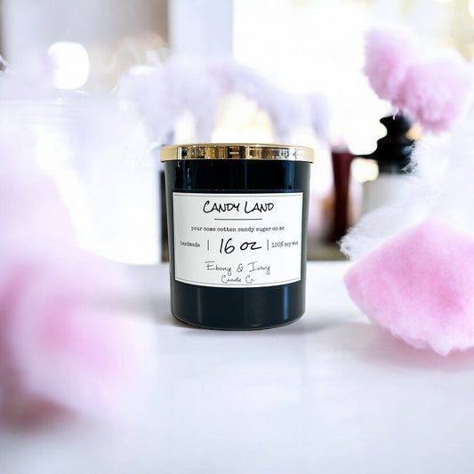 A black 16oz soy candle with a white label named Candy land, surrounded by cotton candy. sweet scent candles Canada fruity tropical candle home fragrance guide