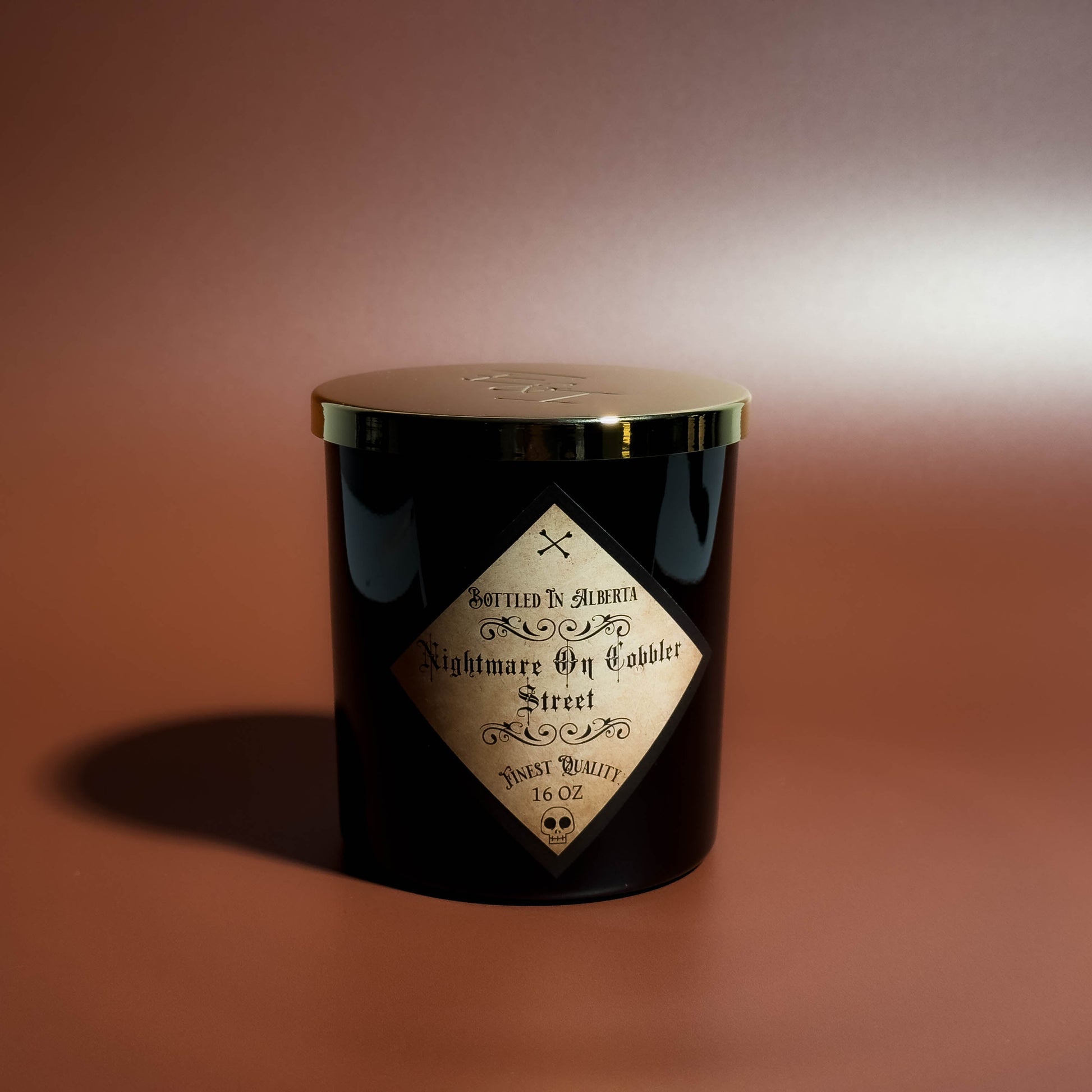 Black candle with a gold lid and label on a brown background