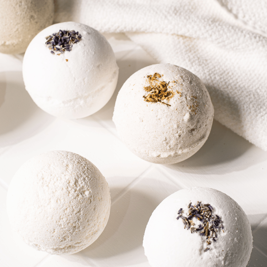 4 white bath bombs, one made with pumpkin powder, two made with lavender buds, and one made with chamomile buds, made by Ebony & Ivory Candle Co in Lethbridge, Alberta, Canada