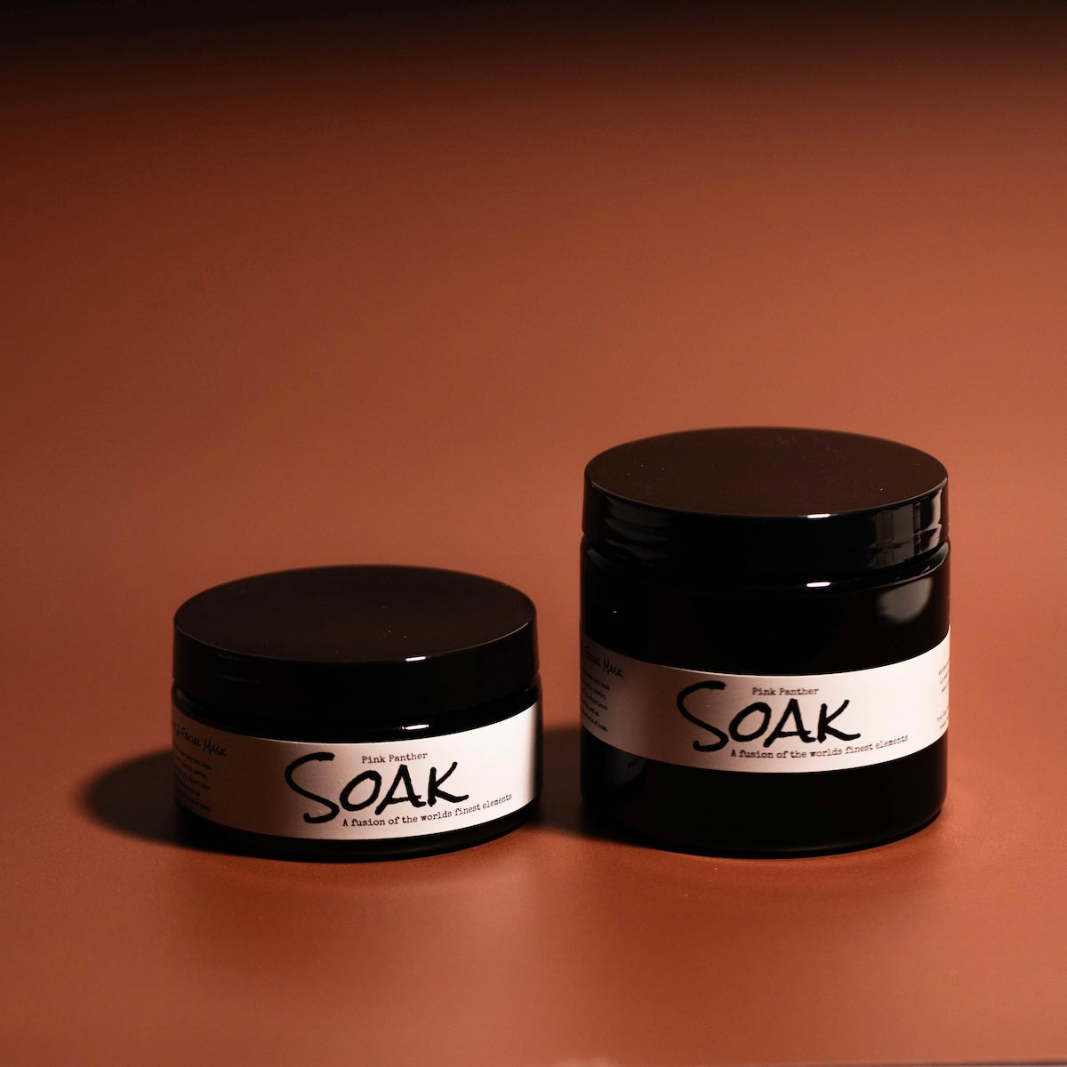 a 4oz and an 8oz round black jars with a white label named Pink Panther Clay Soak, on a red background, made by Ebony & Ivory Candle Co in Lethbridge, Alberta, Canada