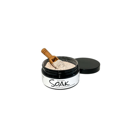 A 4oz round black jar with a white label named Pink Panther Clay Soak, with a wooden spoon, on a white background, made by Ebony & Ivory Candle Co in Lethbridge, Alberta, Canada