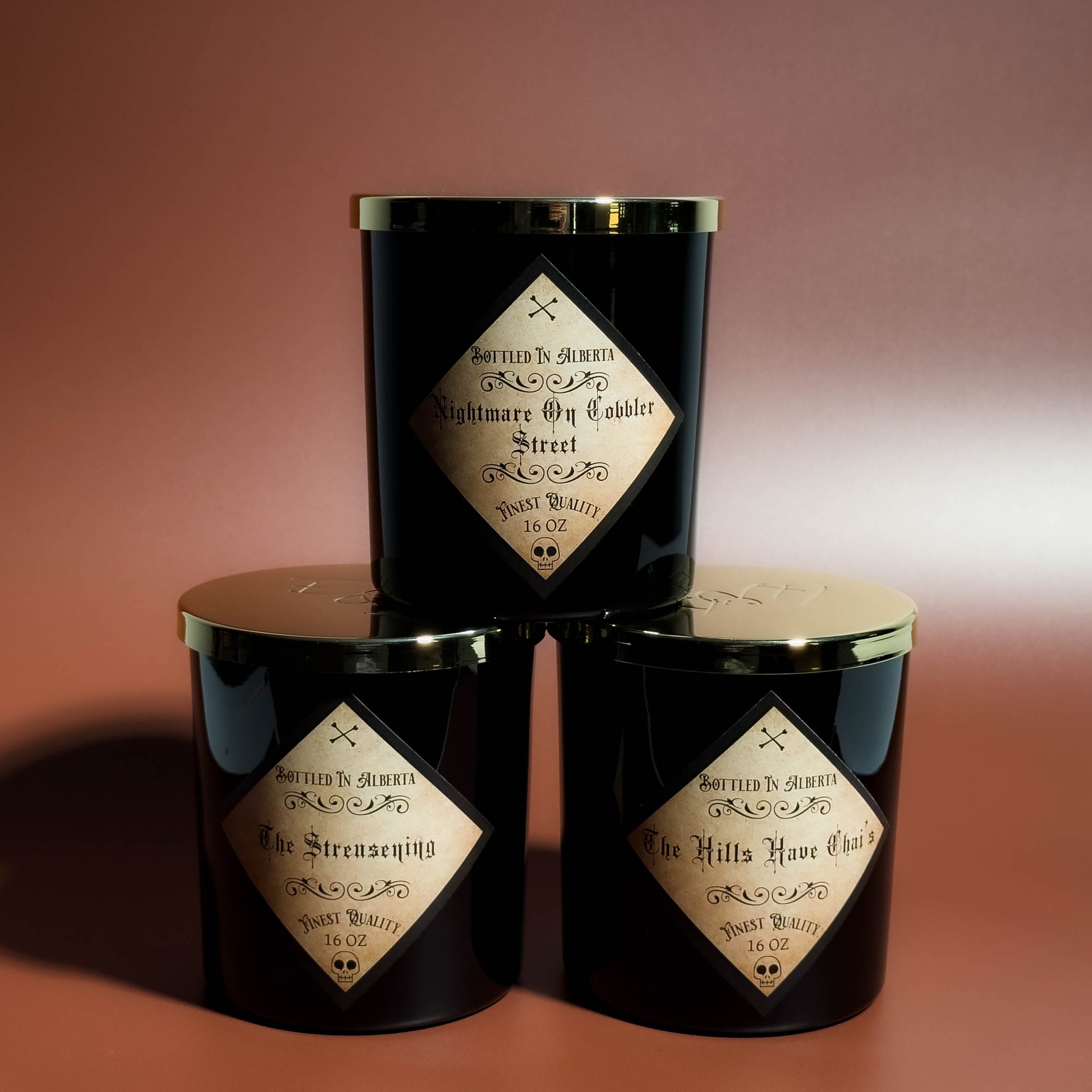 Three black candles with gold accents and decorative labels on a brown background