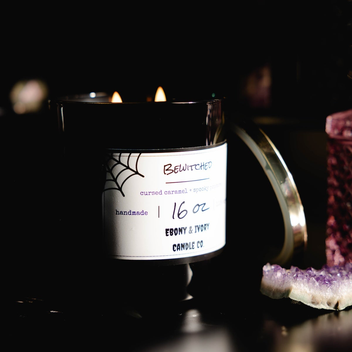 Black 16oz soy Candle with a label on a dark background. Bewitched soy candle for halloween.