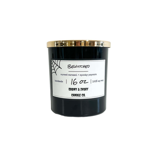 A black 16oz soy candle with a gold lid a white label with cobwebs, named "bewitched," on a white background