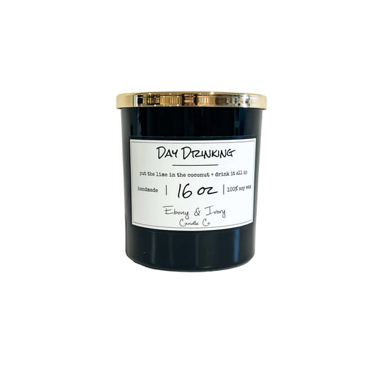 A black 16oz soy candle with a gold lid, labelled Day Drinking, on a white background. Made in Lethbridge Alberta Canada