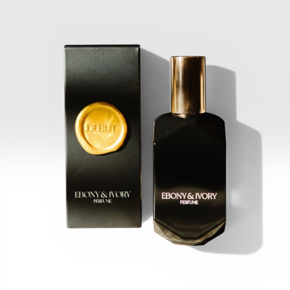 A black Ebony & Ivory luxury perfume bottle with a gold lid sitting next to a black box with a gold wax seal named Debut