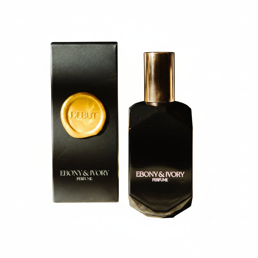 a black geometric perfume bottle made by ebony & ivory candle co in Lethbridge alberta canada, sitting next to it's black box with a gold wax seal label named Debut, on a white background