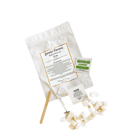 An 8 oz soy candle Almost Famous refill kit with a white back, a white lable, soy wax cubes, an alcohol wipe, a wick, a popsicle stick wick holder, a bottom candle safety label, and a glue dot, on a white background, made by Ebony & Ivory Candle Co in lethbridge, Alberta, Canada