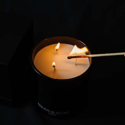 A top down view of a black 18oz jar coconut soy candle being lit with a match, with a white Ebony & Ivory on the front of it with an imprint in the wax that says Dolce, on a black background, made by Ebony & Ivory Candle Co in Lethbridge, Alberta, Canada