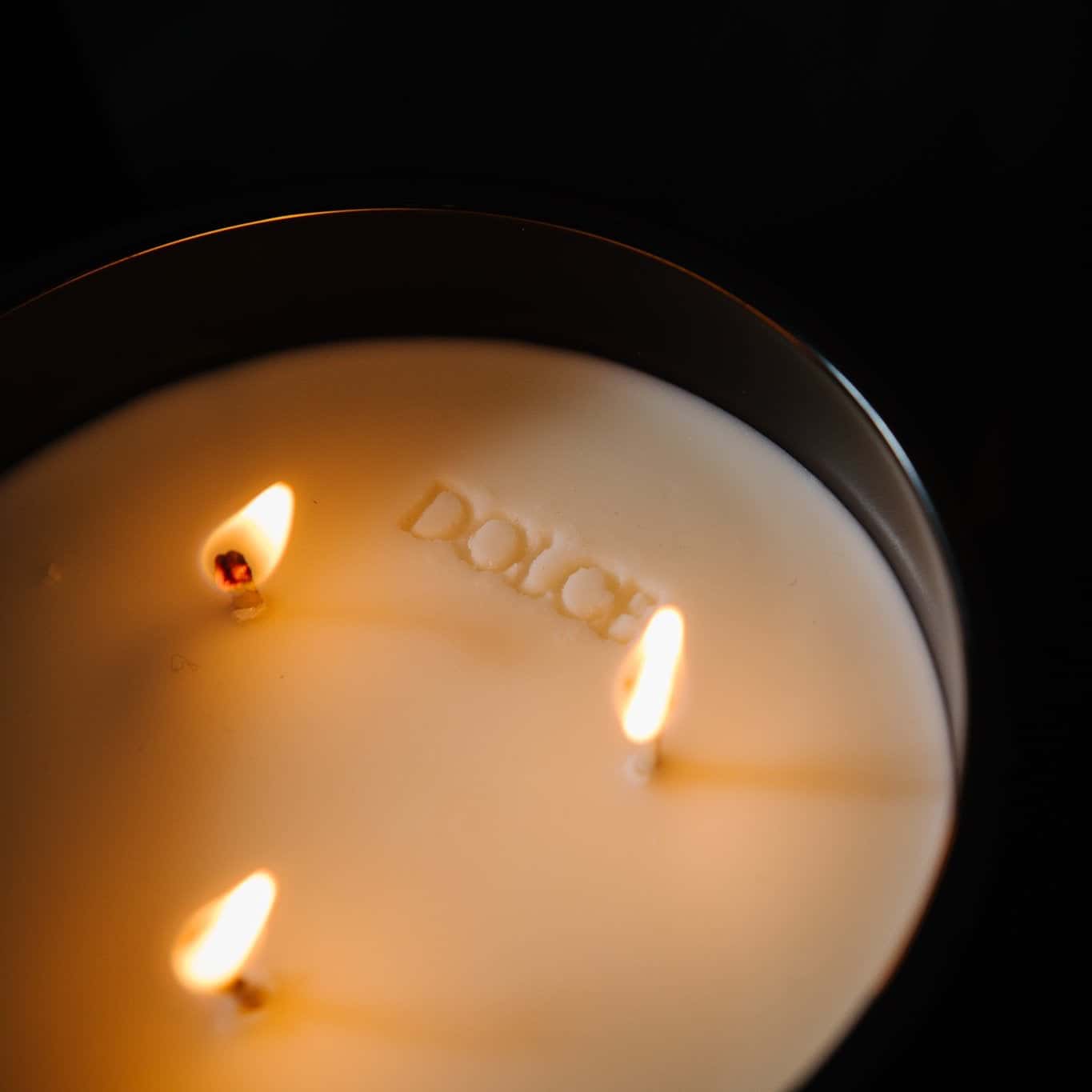 A top down view of a black 18oz jar coconut soy candle, with an imprint in the wax that says Dolce, on a black background, made by Ebony & Ivory Candle Co in Lethbridge, Alberta, Canada