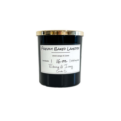 A black 16oz soy candle with a gold lid and a white label named "Freshly Baked Laundry" 