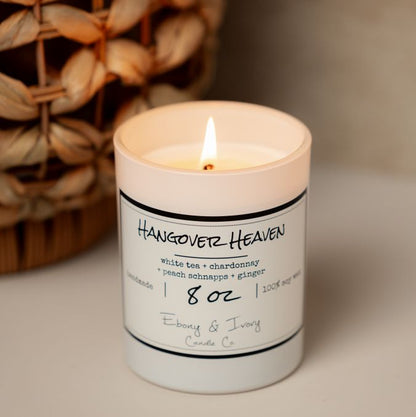 A white 8oz soy candle labelled Hangover Heaven sitting on a table with a wicker basket behind it. Made in Lethbridge Alberta Canada