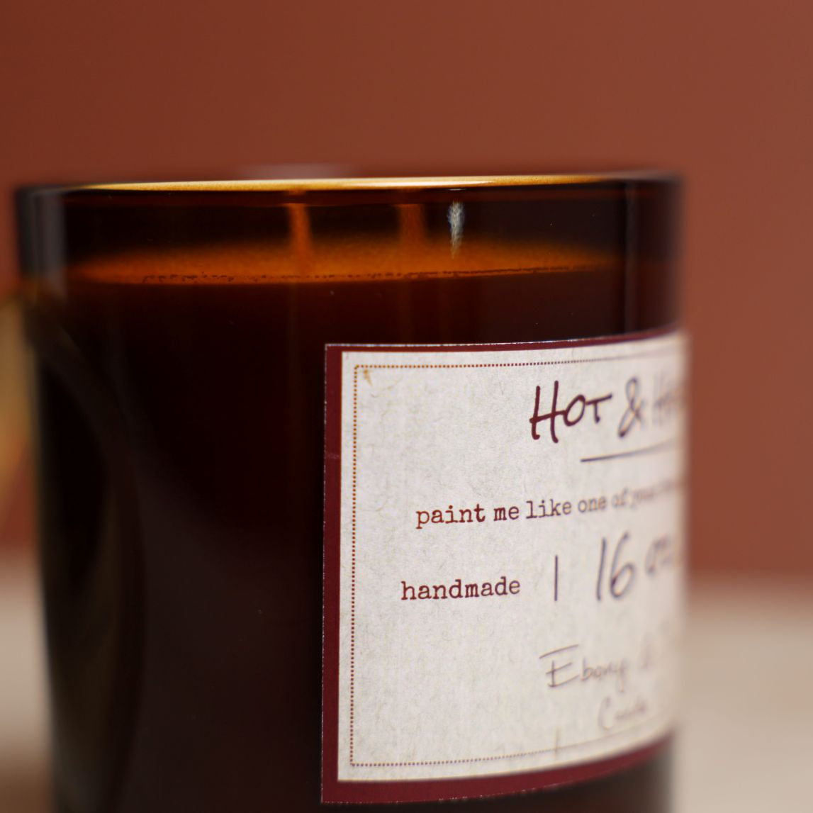 A close up shot of the side of a 16oz soy candle in an amber jar with a lable that reads "Hot & Heavy"
