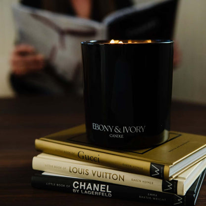 A black 18oz jar coconut soy candle with a white Ebony & Ivory on the front of it, on top of a stack of luxury brand books, made by Ebony & Ivory Candle Co in Lethbridge, Alberta, Canada