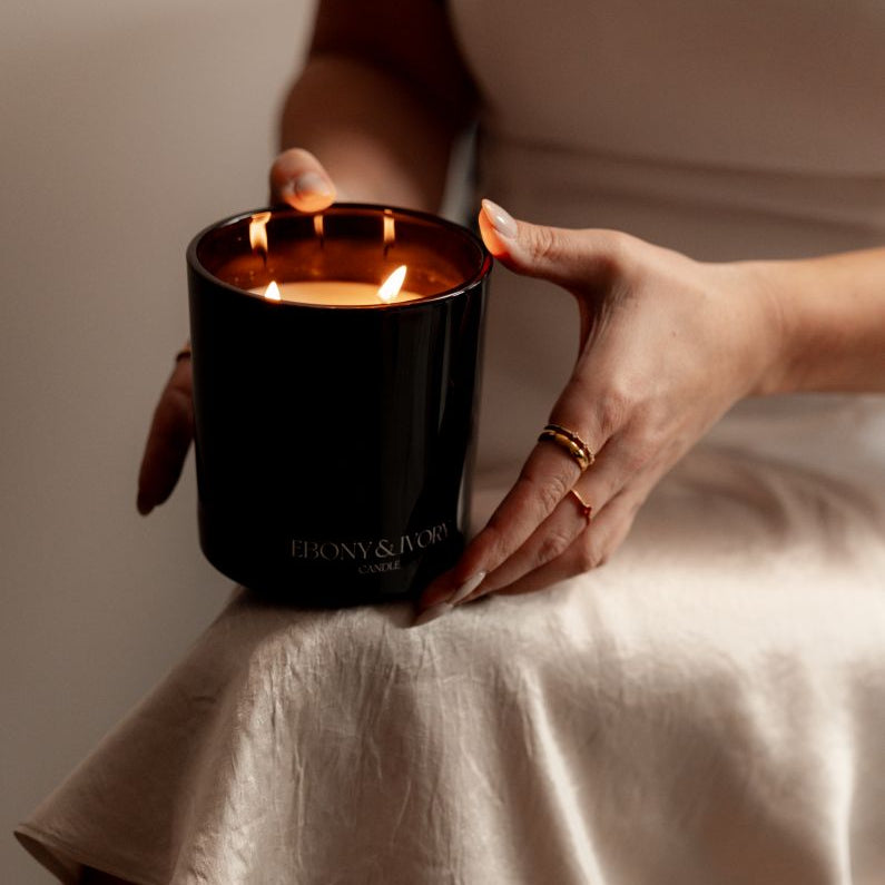 A black 18oz coconut soy candle being held by a woman in a satin skirt. Made by Ebony & Ivory Candle Co in Lethbridge Alberta Canada