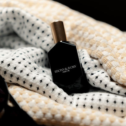 A black perfume bottle with a gold lid nestled in a white and black towel. Made in lethbridge Alberta Canada