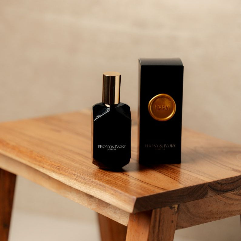 A black perfume bottle with a gold lid sitting on a wooden stool next a black box with a gold wax seal labelled Naria. Made in Lethbridge Alberta Canada