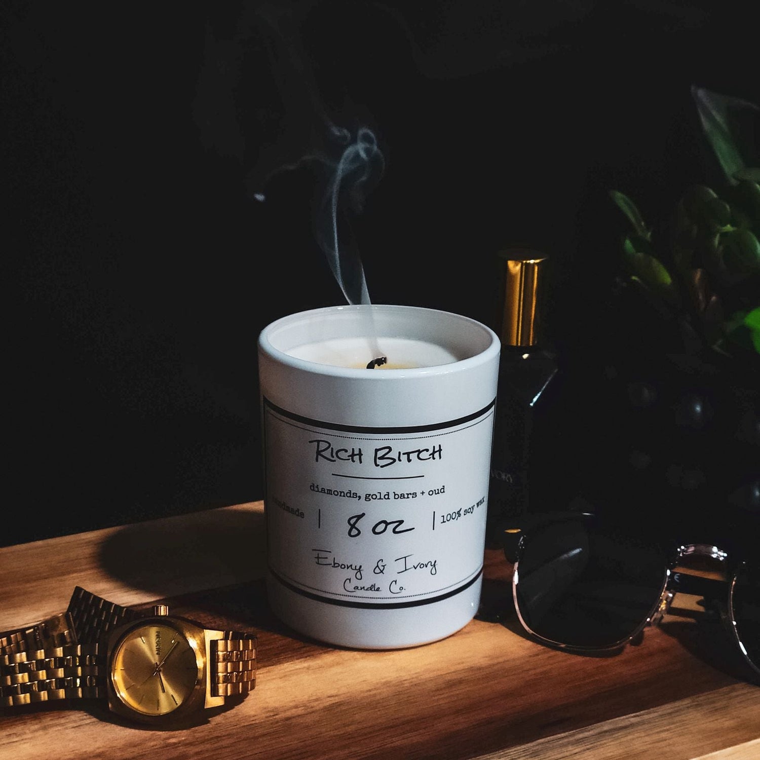 Candle labeled 'Rich Bitch' on a wooden surface with a dark background