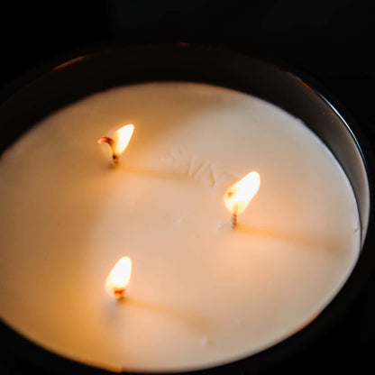 A top down view of a black jar 18oz coconut soy blend candle with the name "Sainy" imprinted on the wax inbetween three lit cotton wicks, on a black background, made by Ebony & Ivory Candle Co in Lethbridge, Alberta, Canada