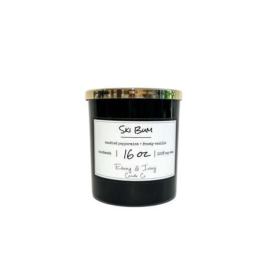 A black jar 16oz soy candle with a gold lid and a white label named Ski Bum, on a white background, made by Ebony & Ivory Candle Co in Lethbridge, Alberta, Canada