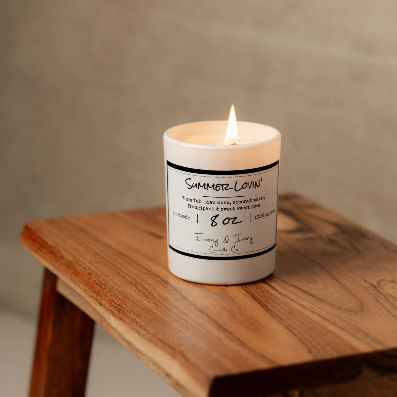 A white 8oz soy candle labelled Summer Lovin, sitting on a wooden stool. Made in lethbridge alberta canada