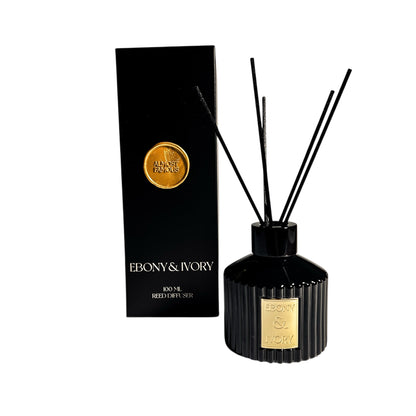 A 100ml black bottle reed diffuser with a gold Ebony & Ivory sticker sits next to a black box with a gold wax Almost Famous wax seal on the front, on a white background, made by Ebony & Ivory Candle Co in Lethbridge, Alberta, Canada
