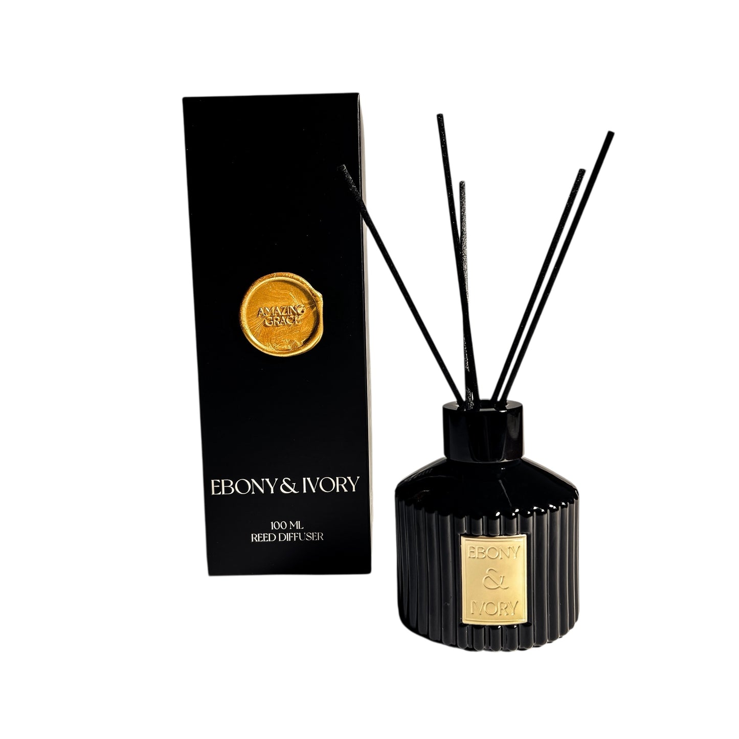 A black 100ml ribbed luxx reed diffuser bottle with black reeds and a gold Ebony & Ivory label, sitting next to a black box with a gold seal named Amazing Grace, on a white background,  made by Ebony & Ivory Candle Co in Lethbridge, Alberta, Canada