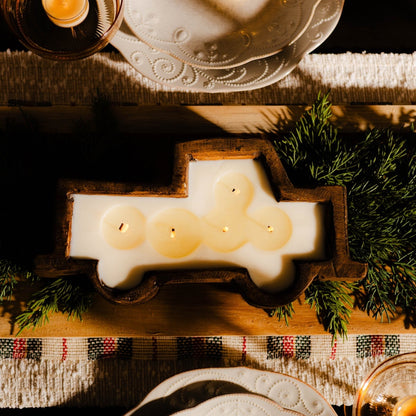 A brown wooden dough bowl candle in the shape of a truck sitting as the center piece of a christmas dining table.