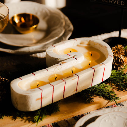 A white and red striped candy cane dough bowl candle sitting as the center piece of a christmas dining table.