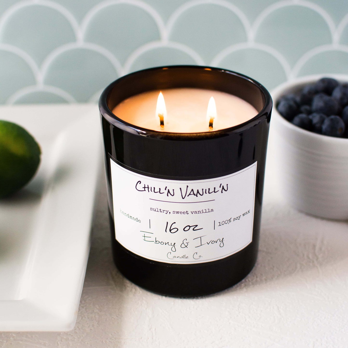 Black 16oz jar soy candle with a gold lid and a white label named Chill'n Vanill'n, on a white kitchen counter, made by ebony & ivory candle co, in lethbridge, alberta, canada