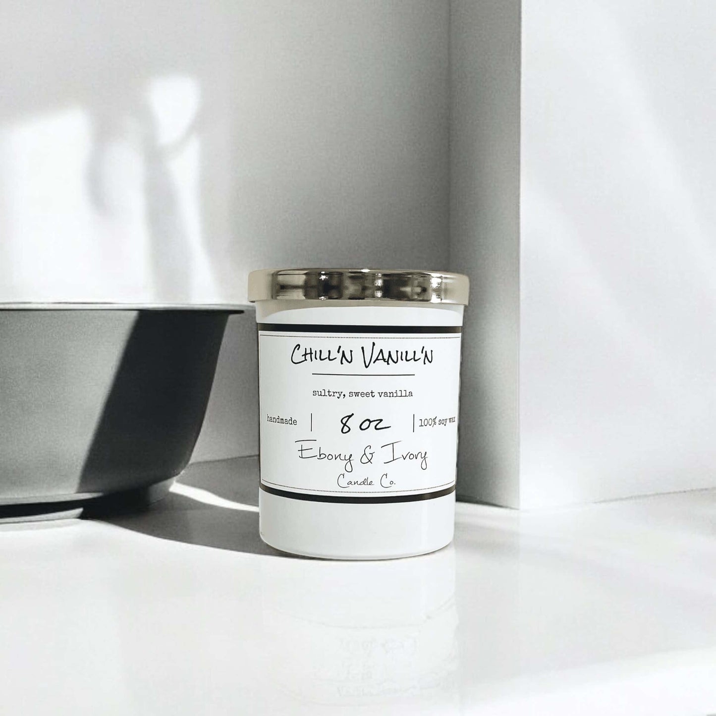 white 8oz jar soy candle with a gold lid and a white label named Chill'n Vanill'n, on a white counter with a grey bowl beside it, made by ebony & ivory candle co, in lethbridge, alberta, canada