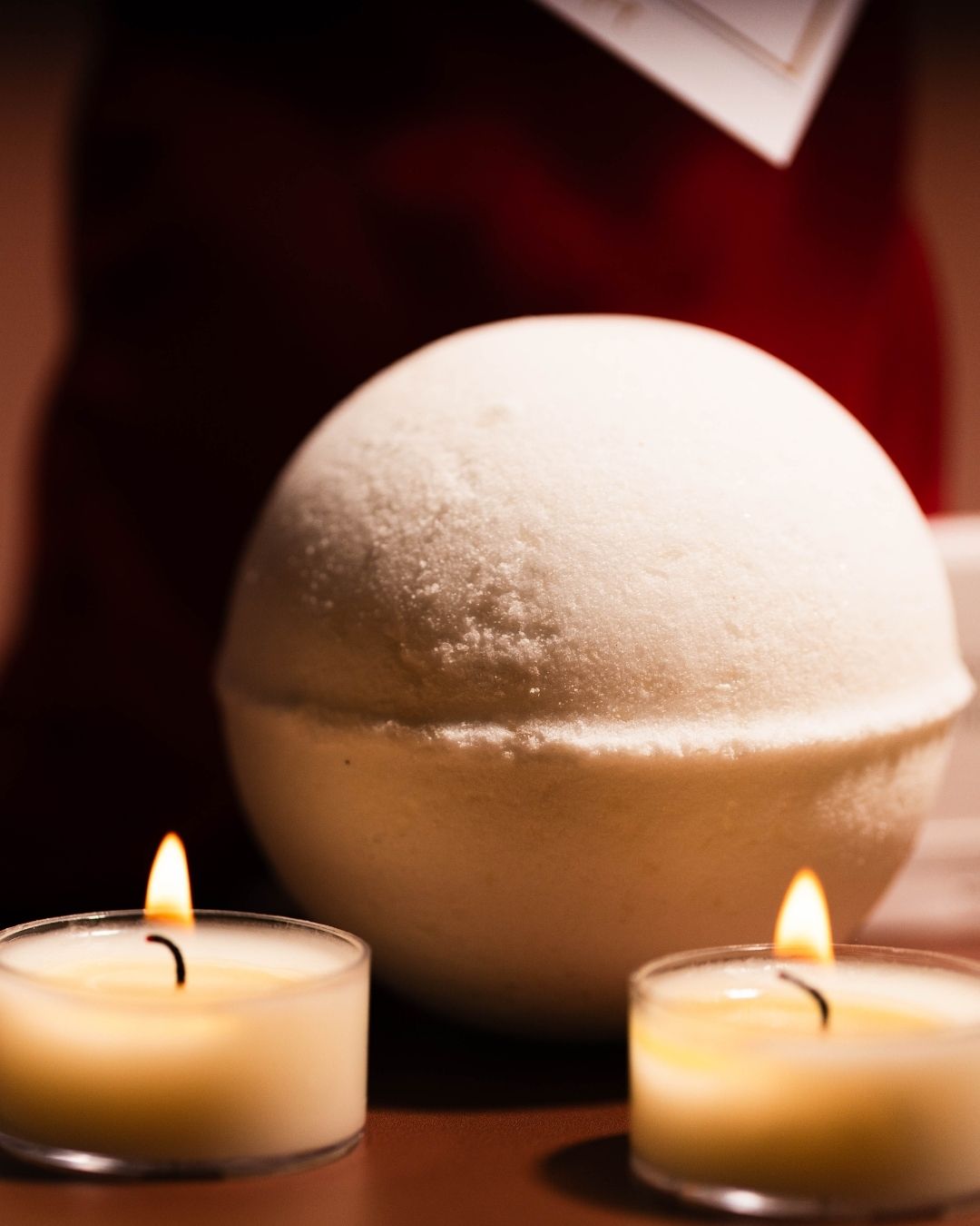 A large bath bomb sitting infront of a red satin bag with tea lights.