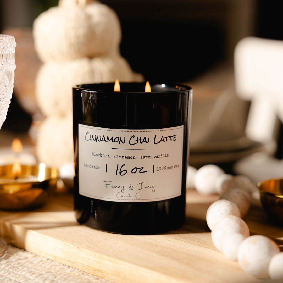 A black 16oz soy candle with a white label named Cinnamon Chai Latte sitting as a center piece on a fall dining table.