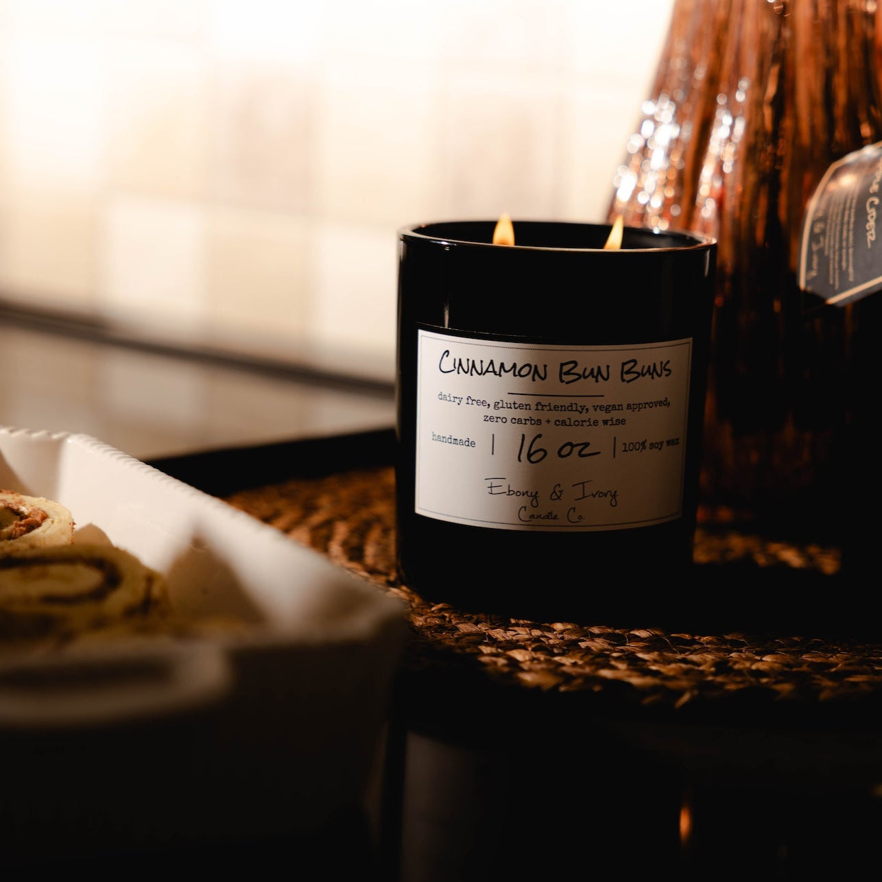 Candle labeled 'Cinnamon Bun'  with a glass spray bottle on a wooden surface. Cozy kitchen decor.