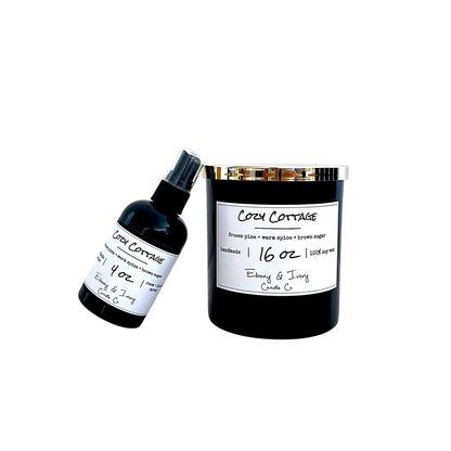A black soy wax candle jar with a gold lid and a white label next to a small black spray bottle, both labeled 'Cozy Cottage' on a plain white background.