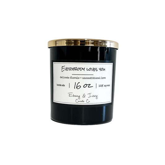 A black 16oz soy candle with a gold lid and label that reads "Everybody Loves You." Made by ebony & ivory candle co in lethbridge alberta canada