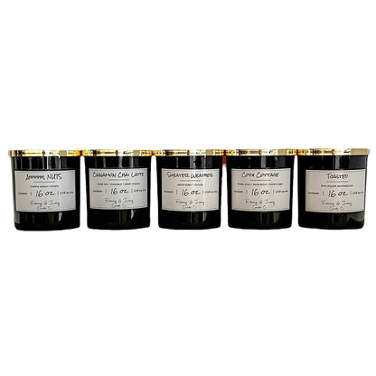 A set of 5 black 16oz soy candles with gold lids and white labels, from left to right they're named "Ahhhhh, NUTS" "Cinnamon Chai Latte" "Sweater Weather" "Cozy Cottage" "Toasted" 