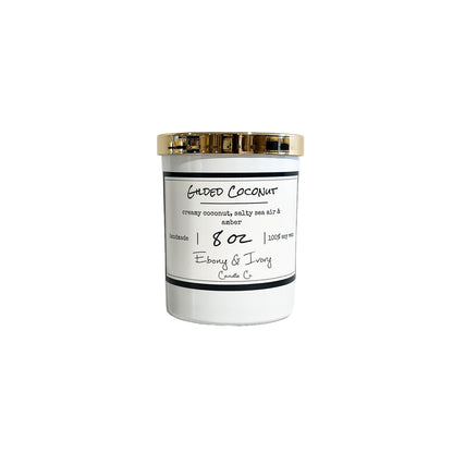 A white 8oz soy candle with a gold lid labelled 'Gilded Coconut' on a white background. Made in lethbridge Alberta Canada