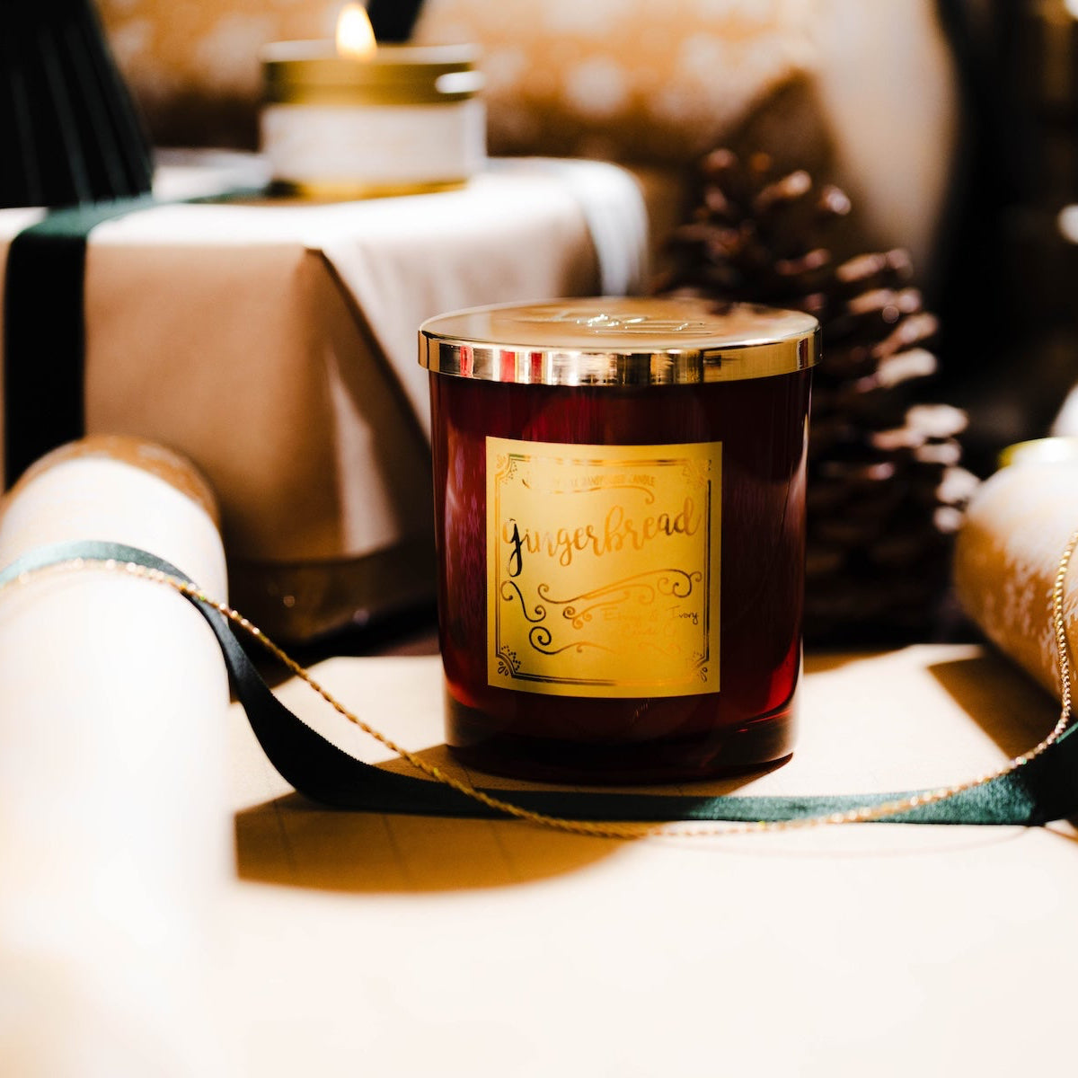 A red 16oz soy christmas candle with a gold lid and a gold label named "gingerbread" sitting on wrapped christmas presents.